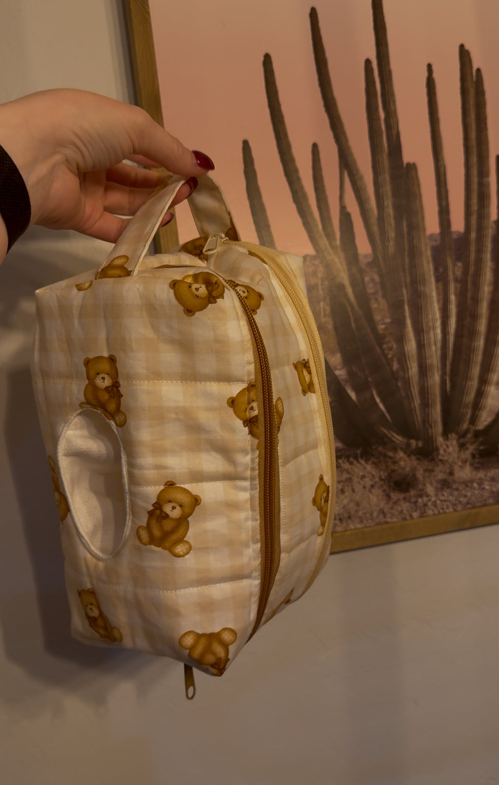 Small bag with teddy bear pattern held by a hand against a cactus plant picture background